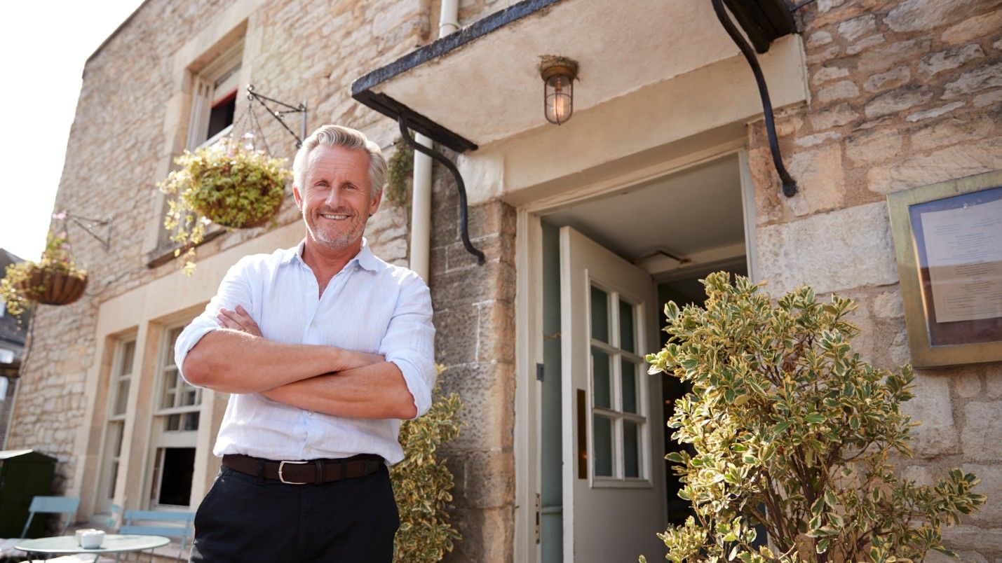 A property manager stands out front of his property with arms folded.