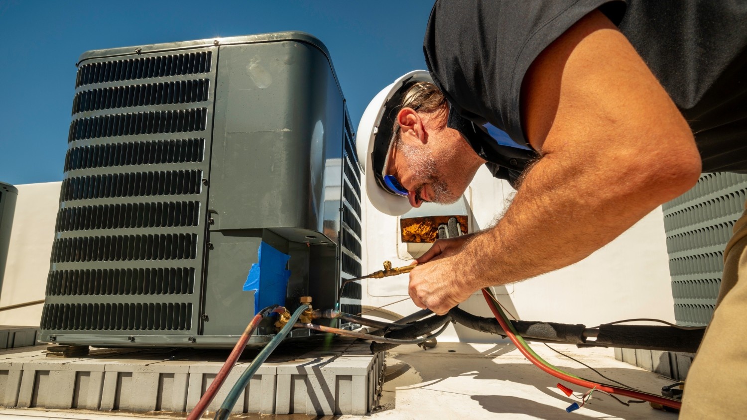 An HVAC technicain in a white hard hat works on a commercial rooftip unit.