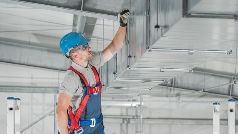 An HVAC tech examines large air ducts in a commercial facility.